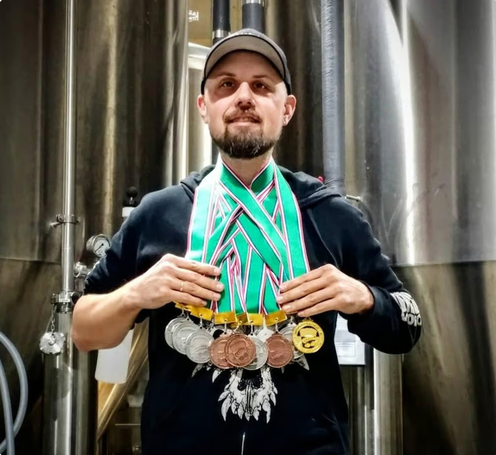 Jason Matthew Kusowski wearing brewing medals in front of brewery tanks